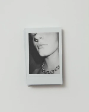 Close-up black and white polaroid showing a person's lower face and thick chain necklace against a white background