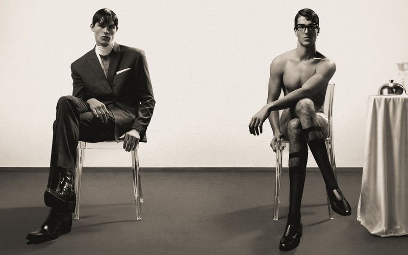 Two male models seated on clear acrylic chairs against a plain background for Numero Netherlands, photographed by Dan-Cristian Gocan.