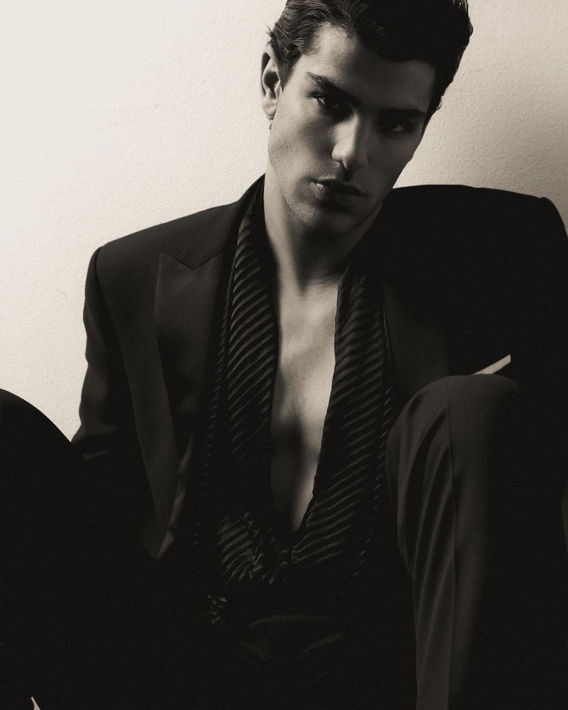 Portrait of a man wearing an unbuttoned dark suit and vest against an off-white background in a studio setting. Fashionable and stylish.
