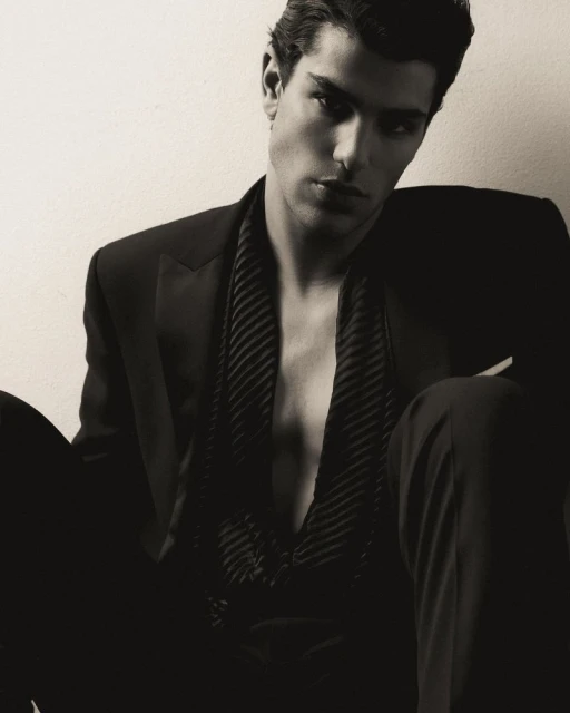 Portrait of a man wearing an unbuttoned dark suit and vest against an off-white background in a studio setting. Fashionable and stylish.