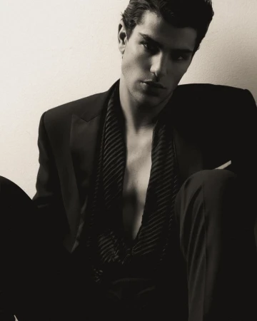 Portrait of a man wearing an unbuttoned dark suit and vest against an off-white background in a studio setting. Fashionable and stylish.