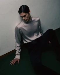 Model Omar Metwally in a satin mock-neck top seated against a wall for Private Protocol by Numero Netherlands, photographed by Dan-Cristian Gocan.