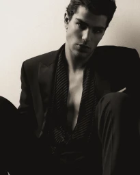 Close-up portrait of a male model wearing a dark suit jacket and striped shirt against a neutral background.
