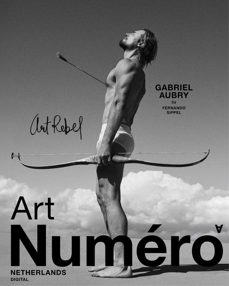 Black and white fashion shot of shirtless man with arrow through chest, holding bow, against bright sky for Numero magazine cover.