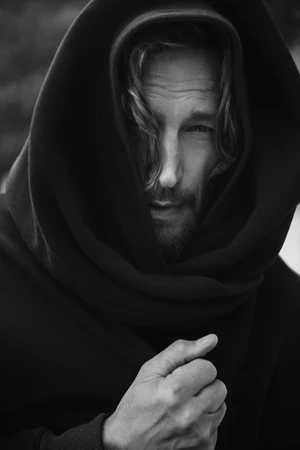 Close-up monochrome portrait of Gabriel Aubry wearing a dark hooded sweatshirt against an outdoor background