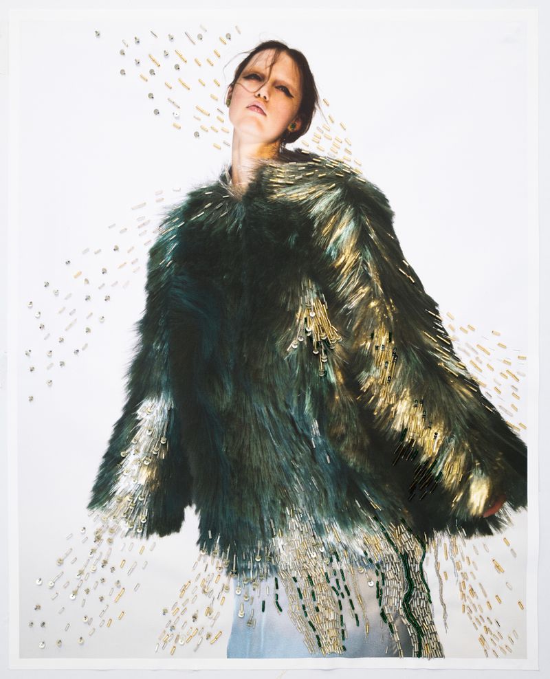Fashion editorial shot of a woman wearing a green and gold faux fur coat on a white background, studio lighting, beads and embellishments.