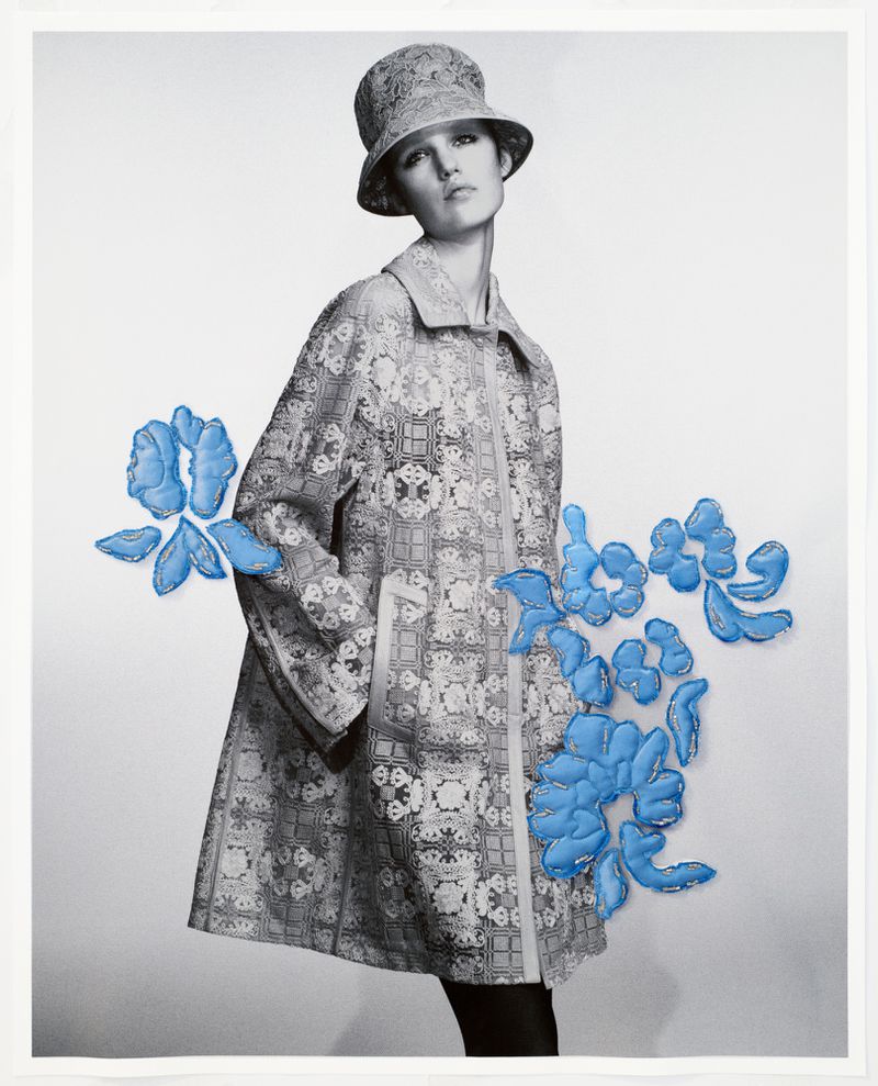 Fashion editorial shot of a female model wearing a patterned coat and hat, standing in front of a white backdrop with blue floral accents.
