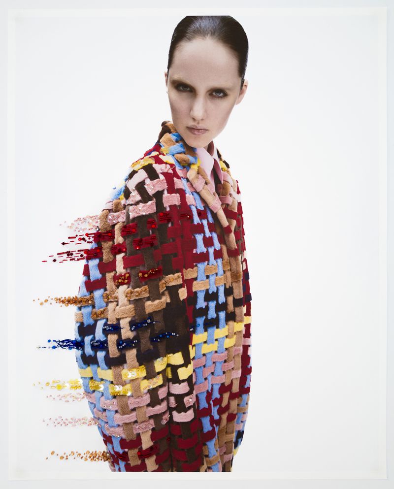 Fashion editorial of a woman wearing a colourful woven jacket in a studio with white background. The jacket has an artful effect.