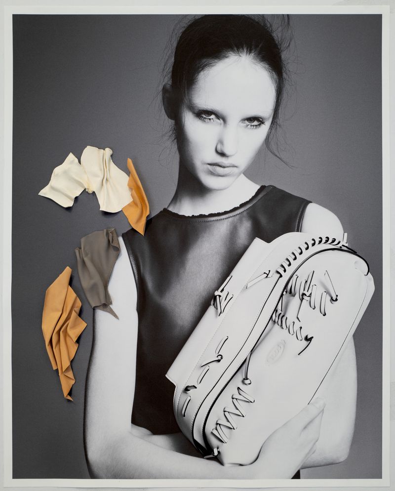 Fashion portrait of a black-and-white woman with fair skin holding a white purse with abstract leather accents and a gray background.