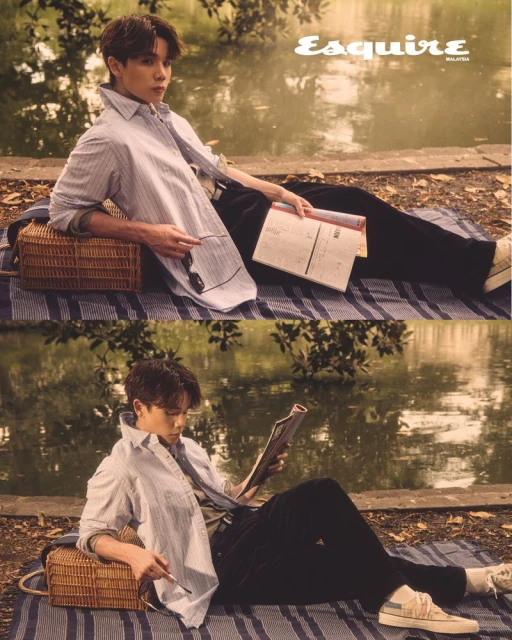 An Asian man sits on a striped picnic blanket by a pond, reading and relaxing, dressed in a striped shirt, for a stylish outdoor fashion editorial.