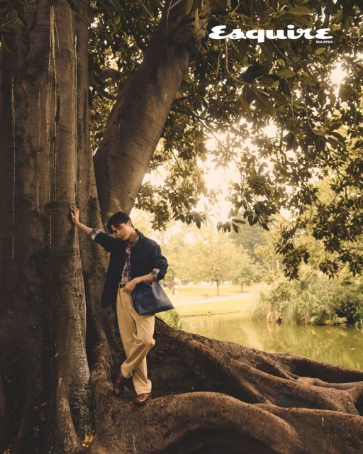 Man poses with a tree for an Esquire magazine cover in a nature setting with a pond and greenery in an eye-level portrait shot.