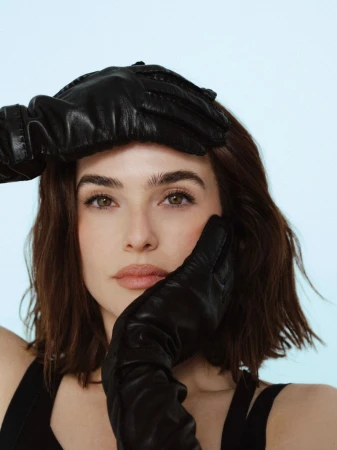 Portrait of Zoey Deutch wearing black leather gloves posing against a pale background for Flaunt.