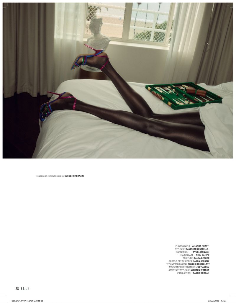Woman's legs elevated on bed with colorful heels and a backgammon game, near a window with sunlight, casting shadows in the room.