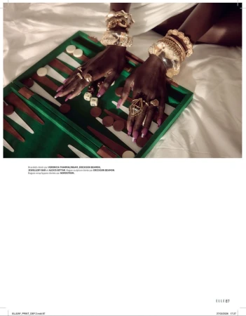 Person's hands adorned with jewelry over a backgammon board on a white bed, showcasing accessories and a lifestyle setting.