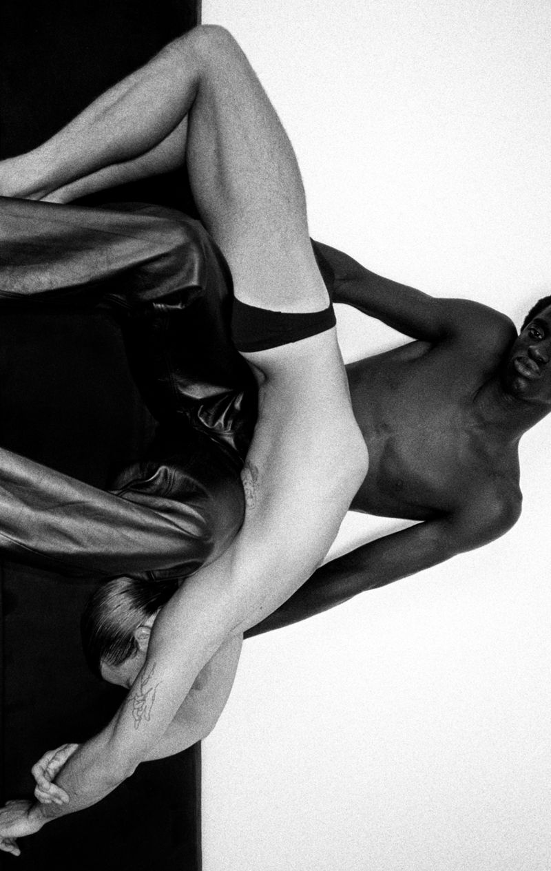 Two shirtless men with different skin tones are positioned against a stark black and white background, highlighting contrast and form.
