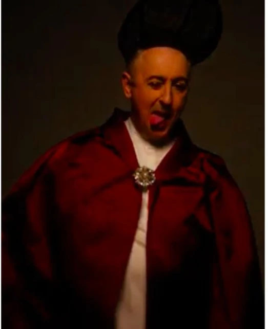 An adult male in a costume with a cape and hat, sticking out his tongue, captured in a studio with dark lighting for a theatrical portrait.