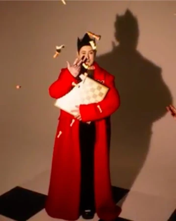 Adult male in a red coat and crown holding a chess board with chess pieces falling around him in a studio setting.