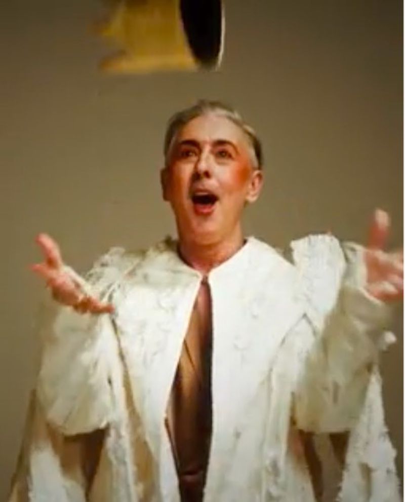 Dramatic portrait of a person with wide eyes and open mouth, wearing a decorative robe, with an object floating above their head.