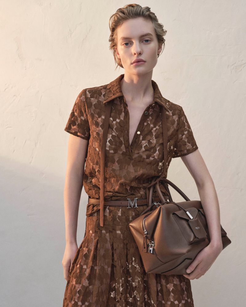Fashionable woman in brown lace dress holding a matching leather satchel purse. Sophisticated style and neutral color palette for fashion shoot.