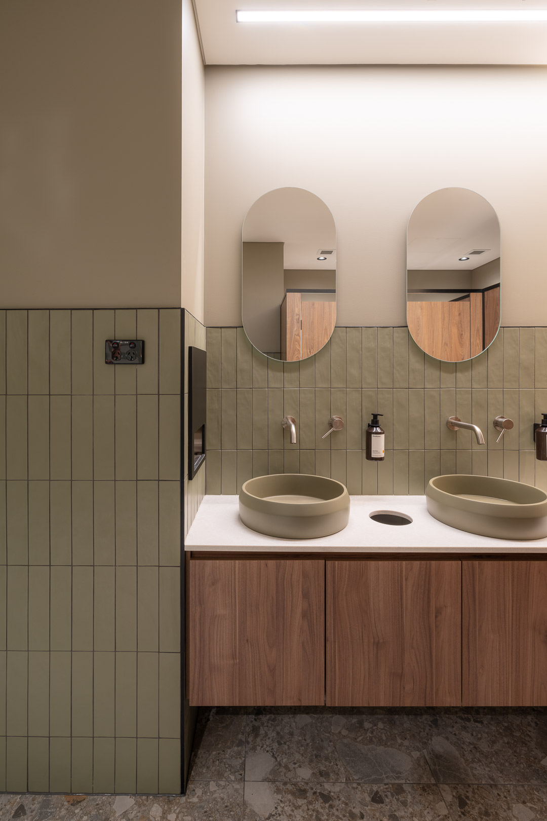 Modern restroom interior featuring two round vessel sinks, twin oval mirrors, and a minimalist design with tile and wooden cabinetry.