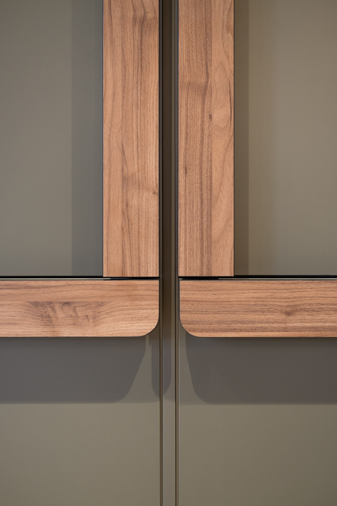 Close-up of sleek, modern cabinet doors in a muted olive green with light wood trim, featuring a minimalist design and subtle shadows.