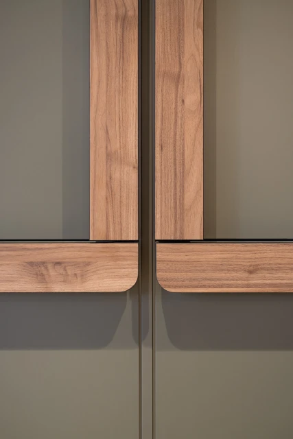 Close-up of sleek, modern cabinet doors in a muted olive green with light wood trim, featuring a minimalist design and subtle shadows.