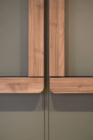 Close-up of sleek, modern cabinet doors in a muted olive green with light wood trim, featuring a minimalist design and subtle shadows.