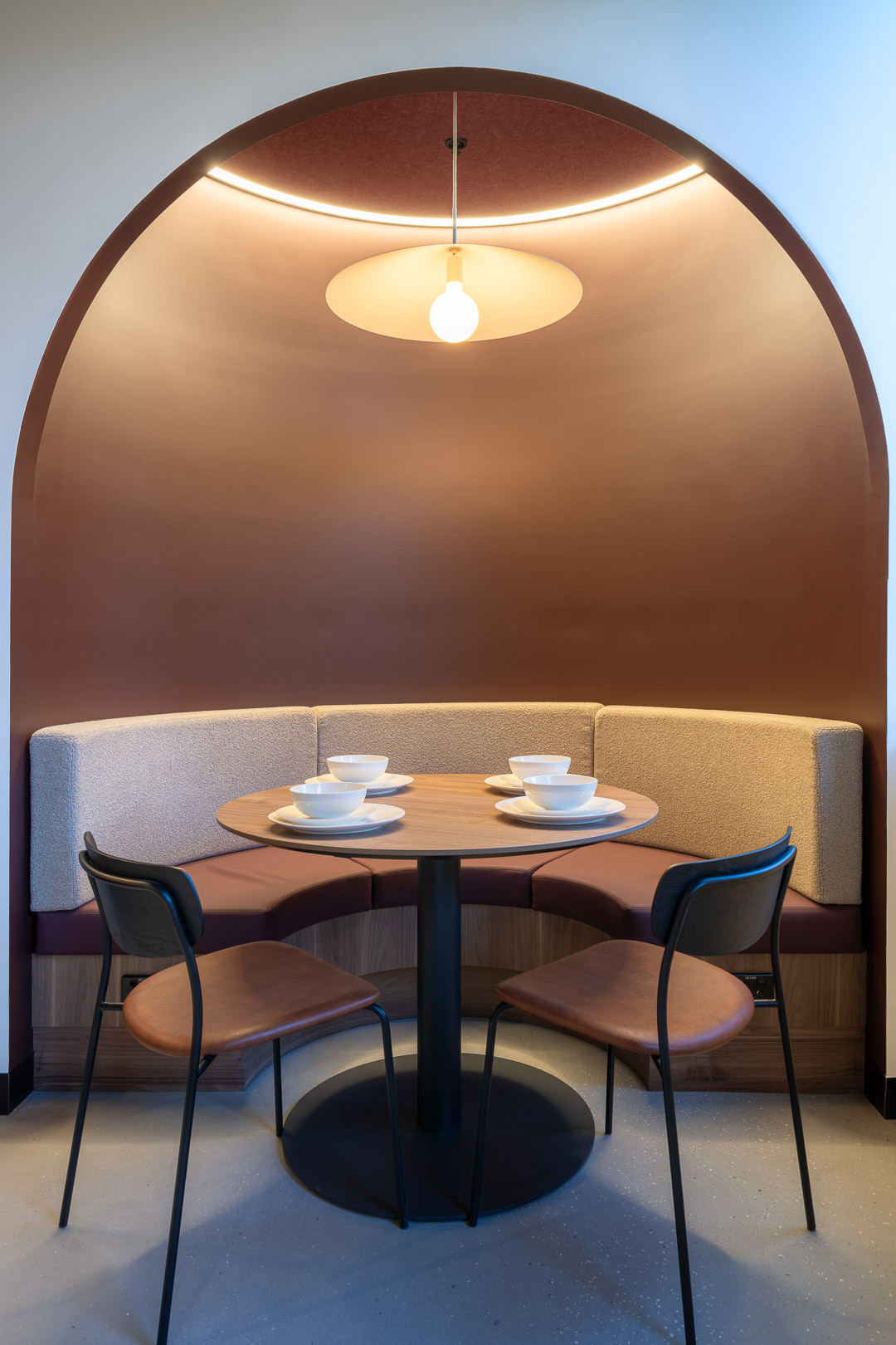 Interior view of cozy alcove with round table, chairs, and built-in curved seating in warm earth tones with modern overhead lighting.