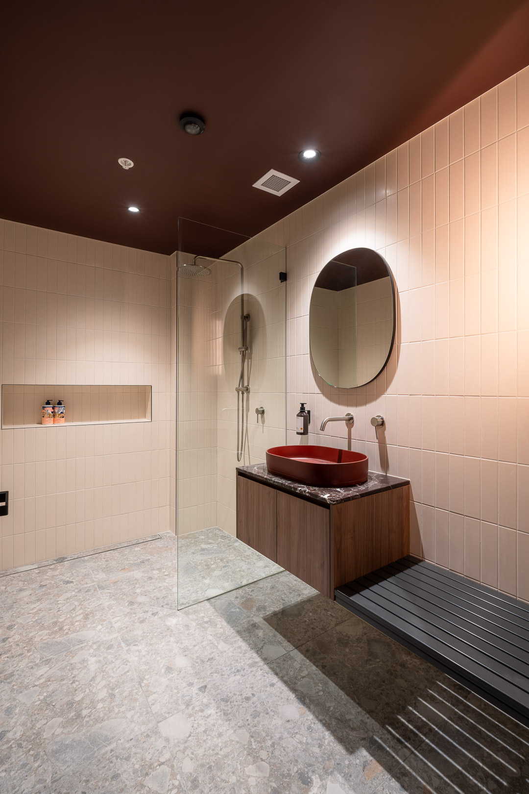 Modern bathroom interior featuring a shower, sink with vanity, large mirror, tiled walls, and a dark brown ceiling, creating a sleek design.