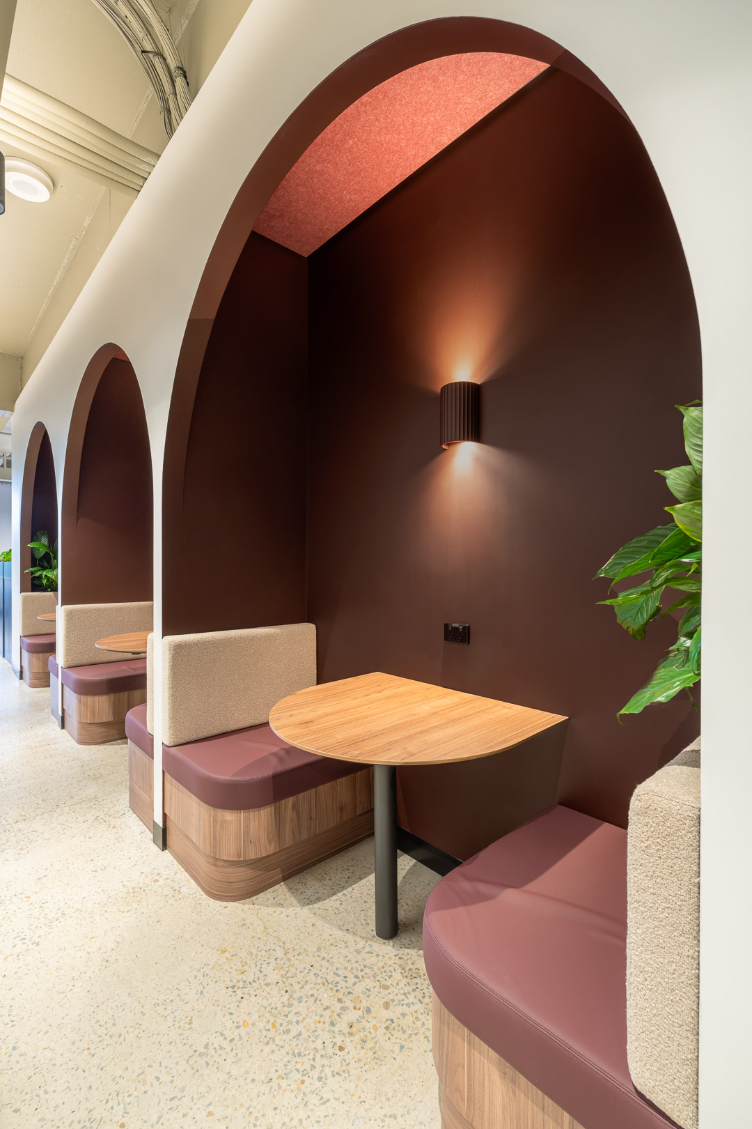 Interior view of modern office nook featuring curved seating, wooden tables, ambient lighting, and dark brown and beige color scheme.