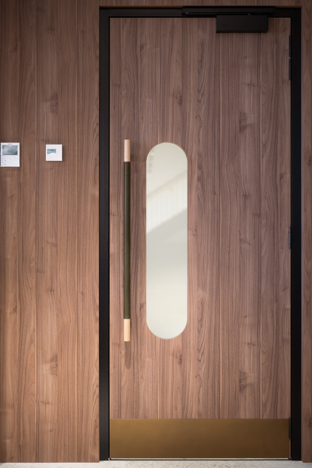 Modern interior featuring a brown wood door with a minimalist design and a long, vertical handle, set against a matching wood wall.