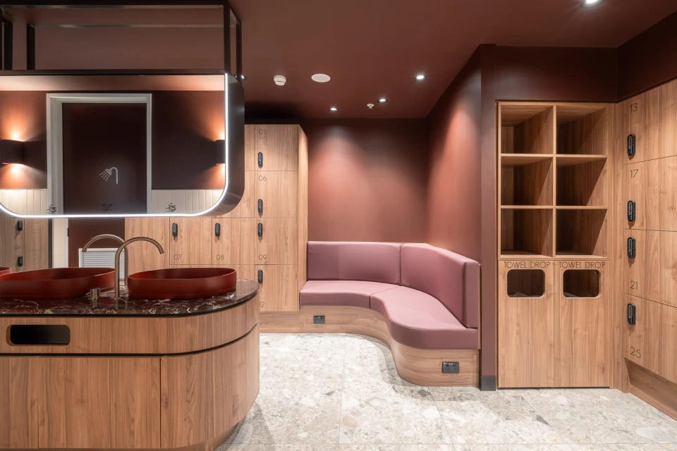 Stylish changing room with cherrywood lockers, red sink basins, and a pink cushioned bench for a modern, luxurious, and functional space.