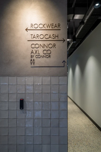 Interior signage on a grey tiled wall points visitors to Rockwear, Tarocash and Connor/AXL Co in a modern building.