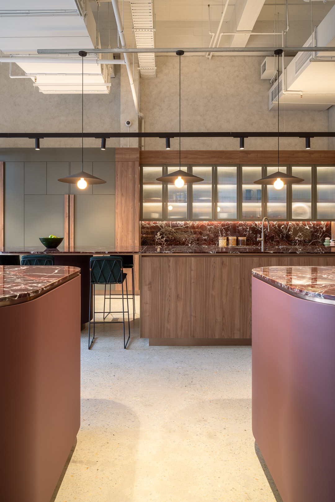 Modern kitchen interior with marble-topped counters, wooden cabinets, pendant lighting, and a minimalist design aesthetic. No people visible.