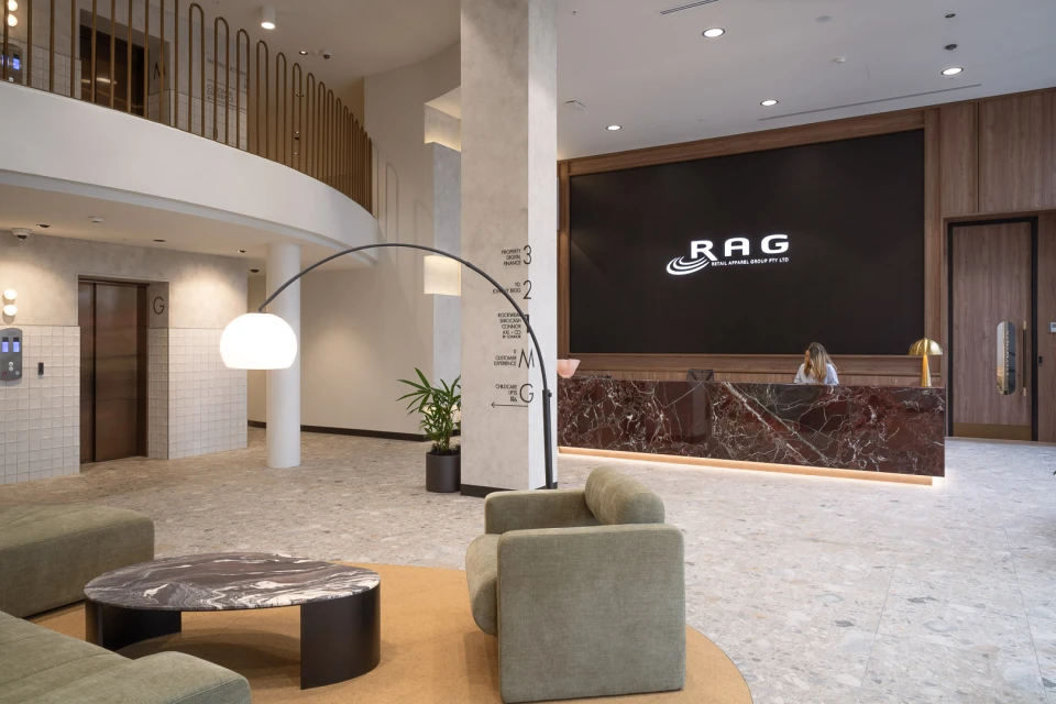 Lobby interior featuring modern seating, marble accents, and a receptionist behind a counter with the RAG Retail Apparel logo.