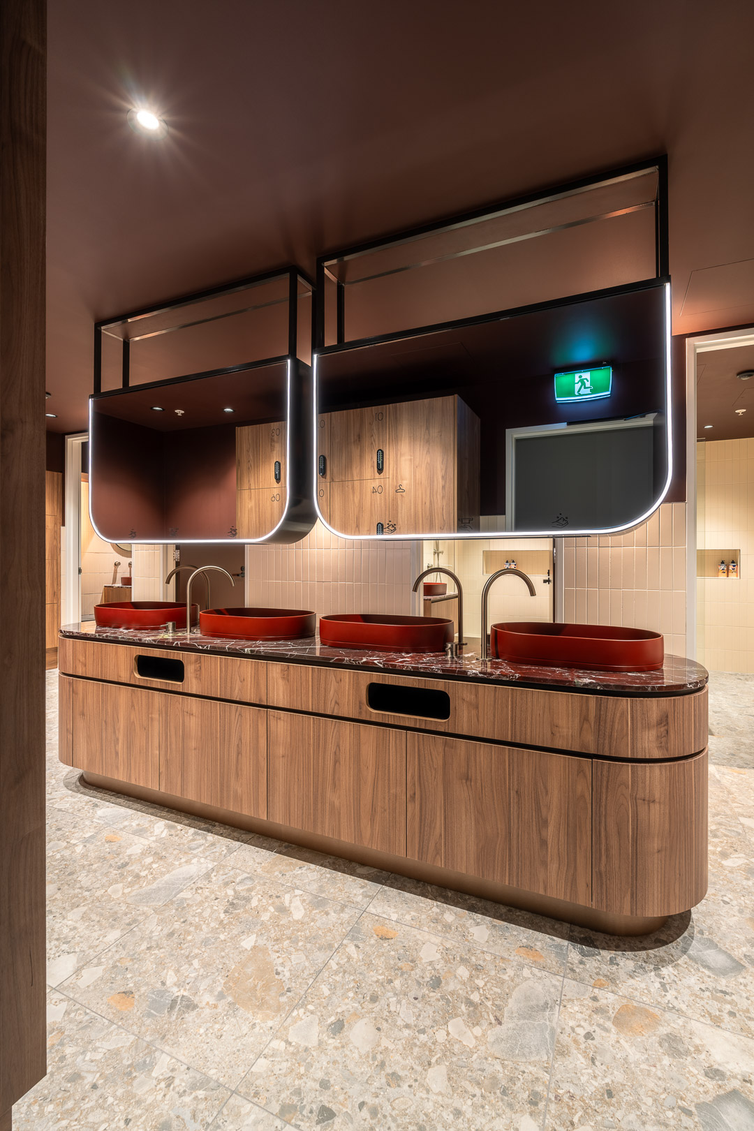 Contemporary public restroom featuring red vessel sinks on a wooden countertop with terrazzo flooring and mirrors with LED lighting.