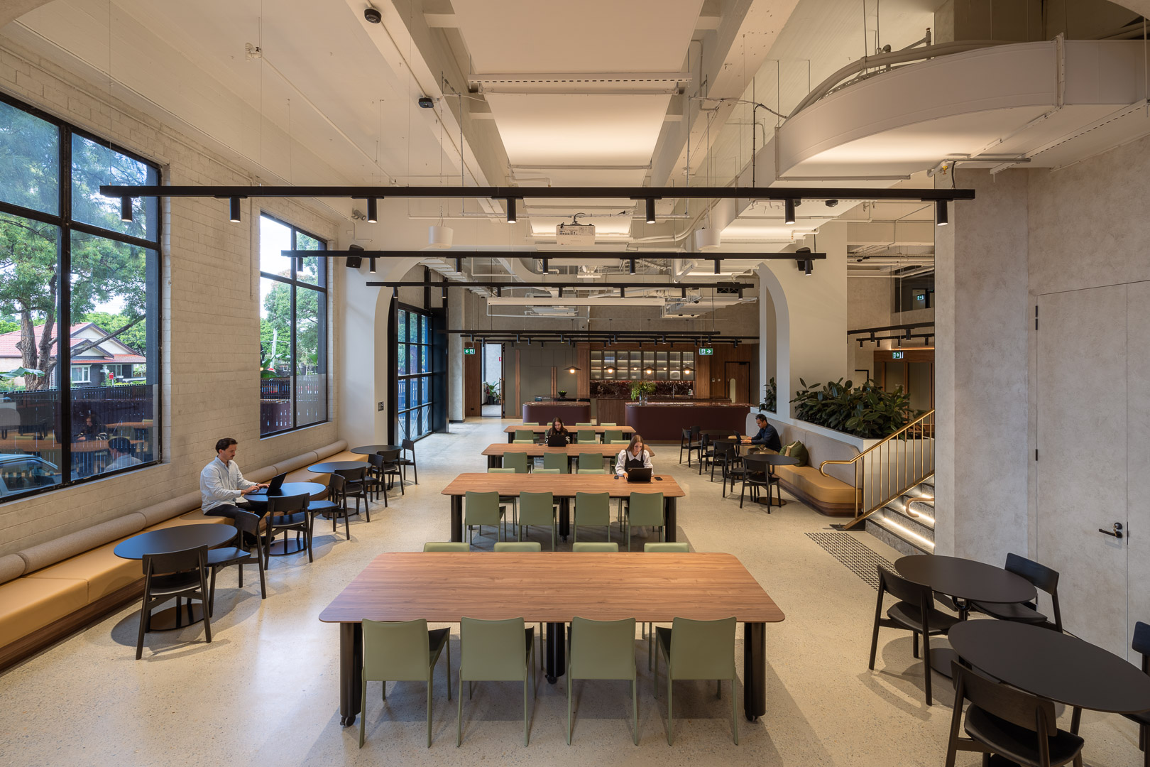 Open workspace featuring a large room with tables and chairs, large windows, and people working on laptops in a modern interior.
