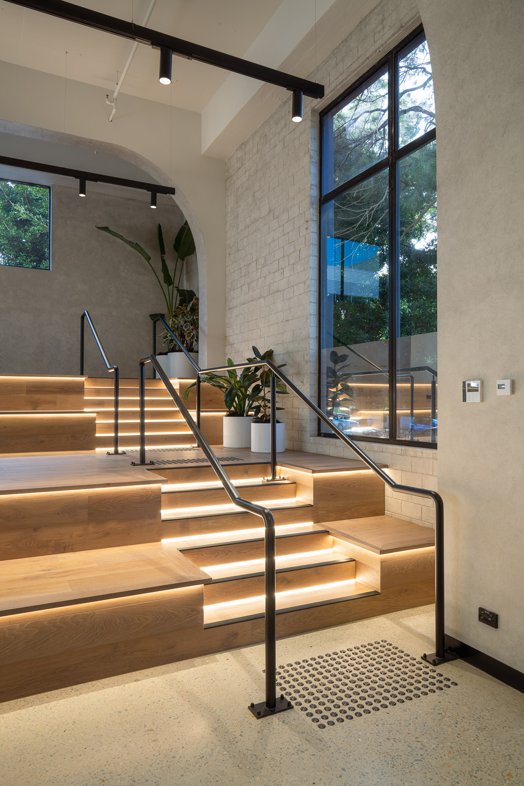 Modern interior staircase with wood steps, black metal railing, and indirect lighting in a bright architectural setting.
