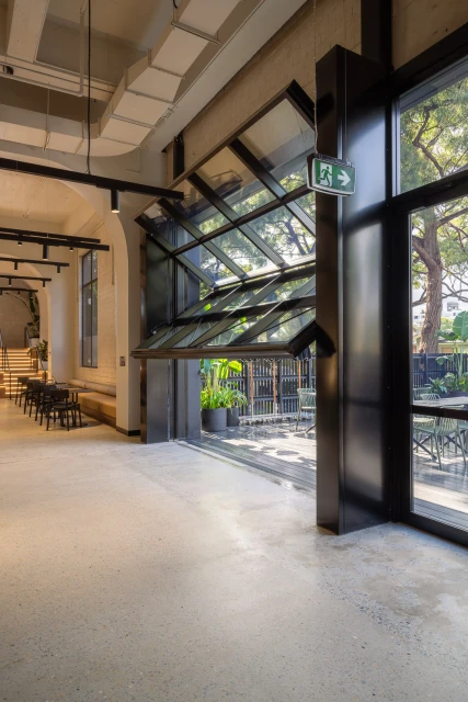 Indoor architectural shot featuring a modern cafe interior with an open view through folding glass doors to an outdoor seating area.