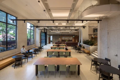 Wide interior view of a spacious modern office workspace featuring wooden tables, green chairs, and large windows by Daniel Cook for Intermain.