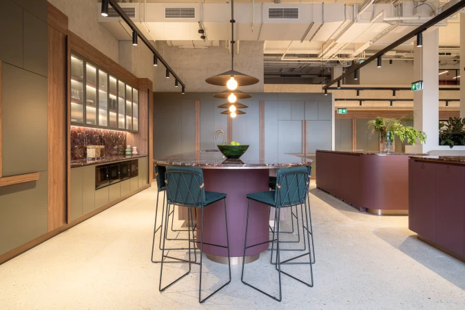 Spacious modern commercial kitchen interior with a central curved island counter, dark teal bar stools, and track lighting.