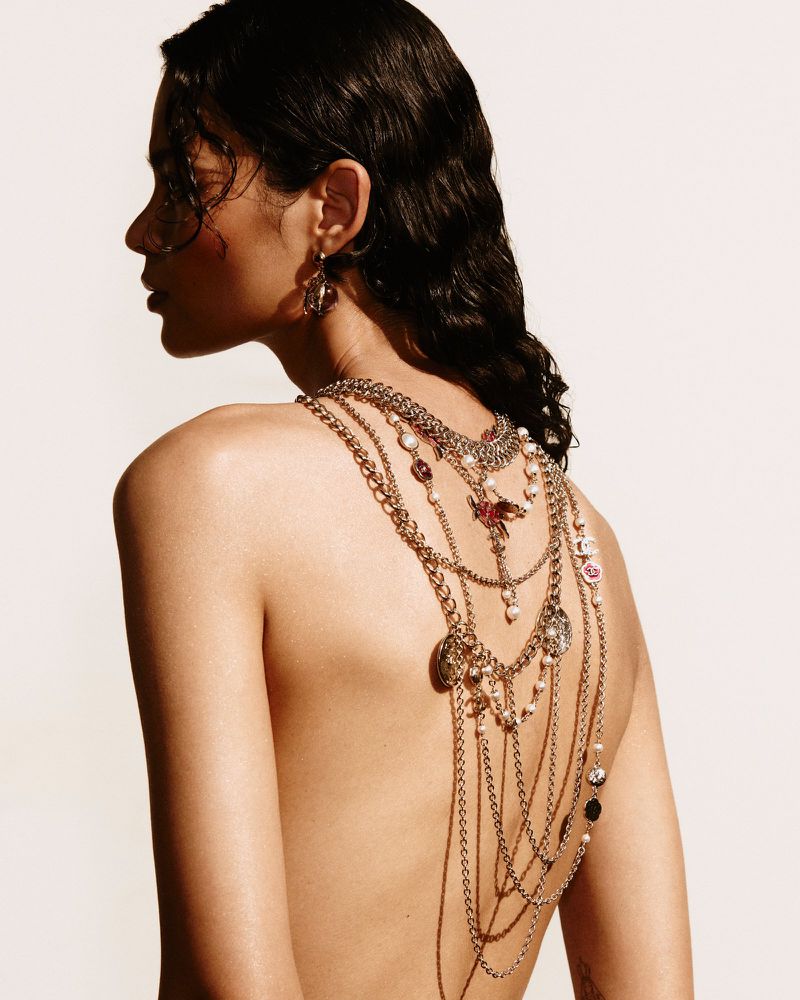 Adult female with dark curly hair faces away from the camera, adorned with statement jewelry against a clean, bright backdrop.