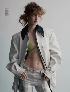 Model wearing an open white jacket with a black collar, green top, and distressed light pants against a plain background