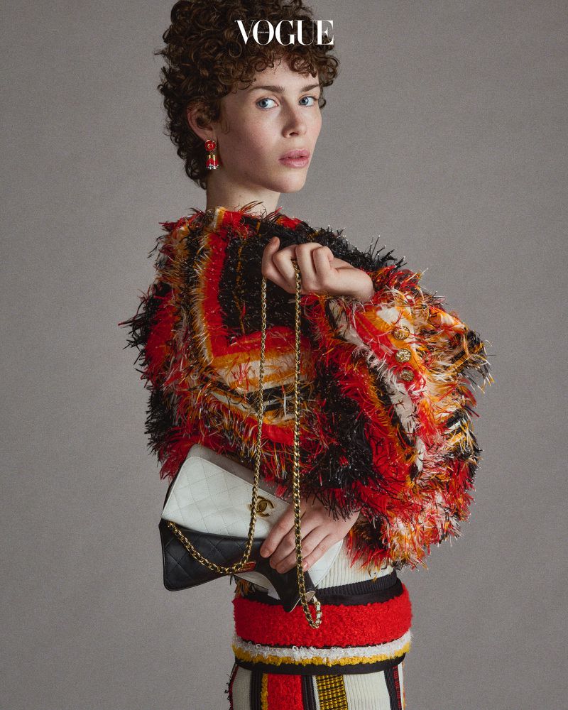 Vogue cover featuring a model with short curly hair wearing a colorful, textured jacket and skirt, holding a Chanel handbag against a grey background.