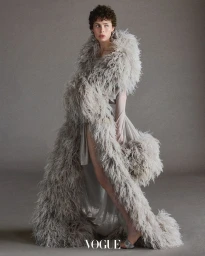 Model in voluminous feather stole and gown posing against a grey seamless backdrop for Vogue Thailand