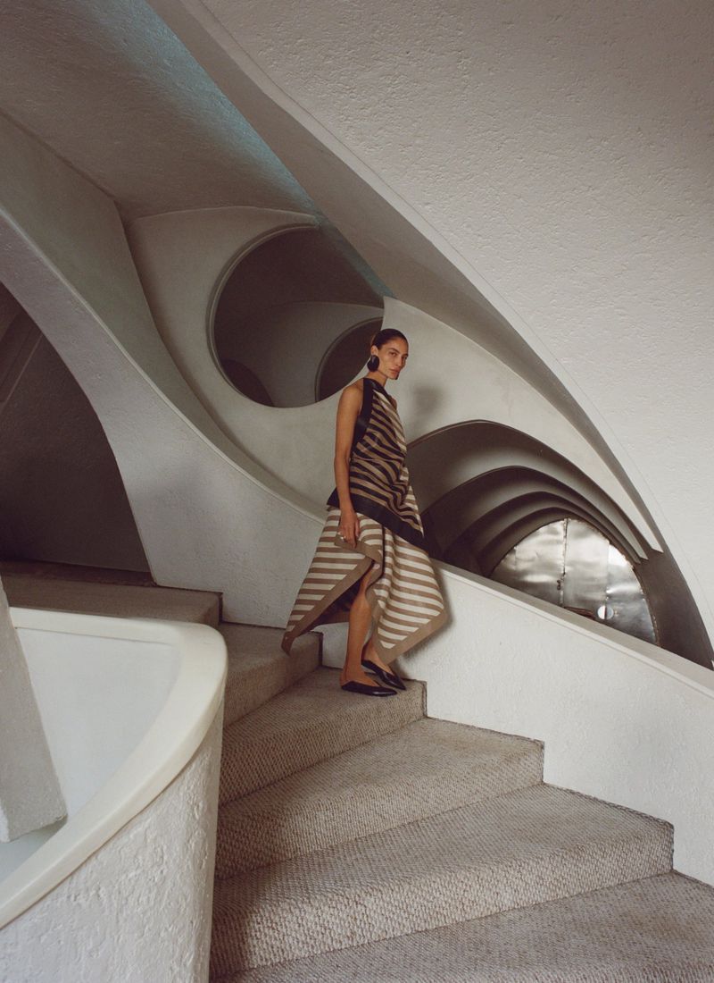 Woman wearing a striped dress walks down carpeted steps inside a building featuring white walls and curving architectural details.