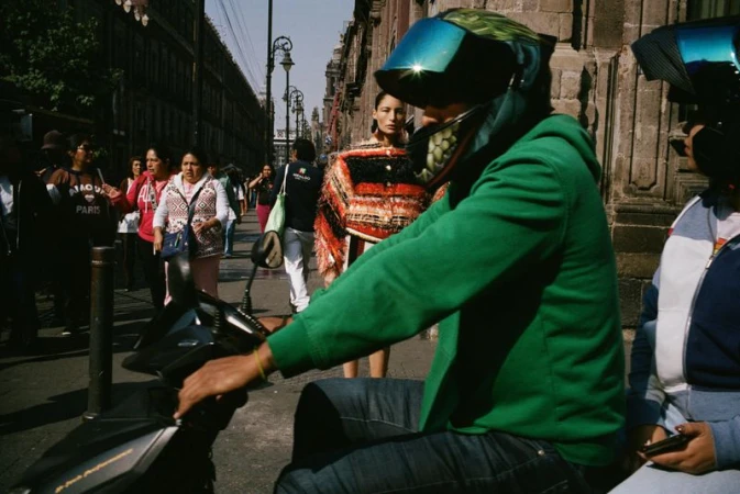 Person in a bright green hoodie wearing a motorcycle helmet on a scooter on a busy street.