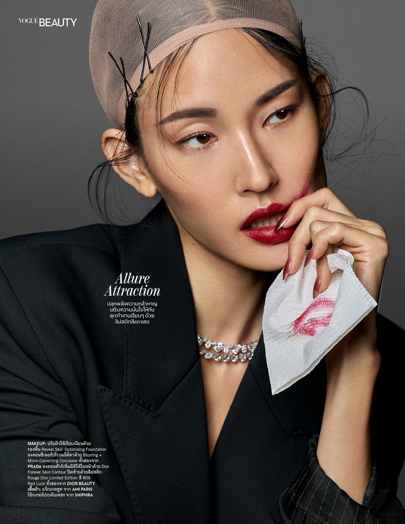 Asian woman in beauty editorial with dark red lipstick, black blazer, and hair net. She is holding a white tissue with lipstick marks.