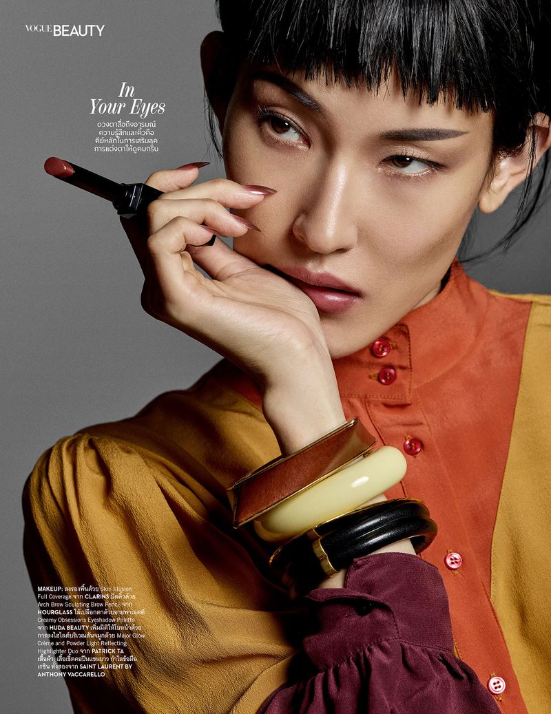 Asian woman in vogue beauty editorial with bold makeup, lipstick and bracelets. High fashion beauty shot against a grey backdrop.