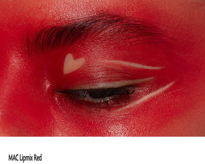 Close-up of a person's eye with red face makeup and white heart and lines makeup design.